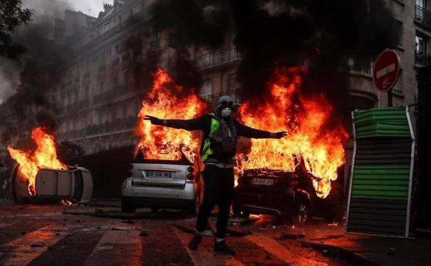 Un manifestante protesta por junto a varios coches en llamas, en París.