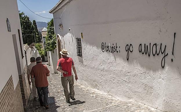 Turistas pasean junto a una pintada que les invita a irse de la ciudad