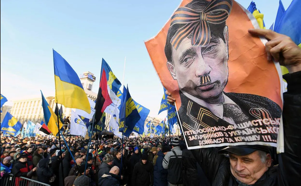 Un manifestante ucraniano sostiene una pancarta donde compara a Putin con Hitler.