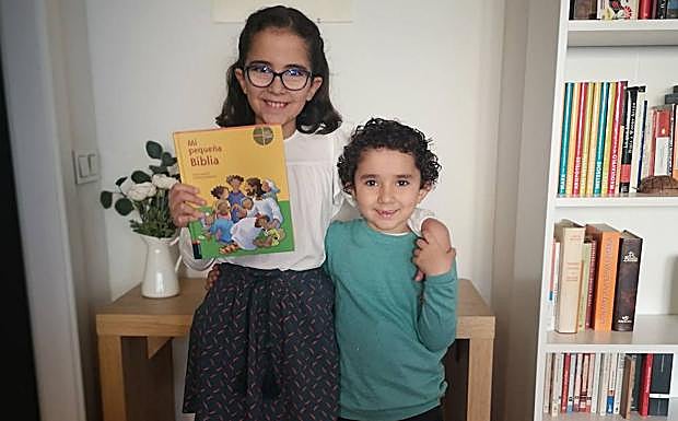 Ana, con su hermano Pablo, sostiene un ejemplar de 'Mi pequeña Biblia'. 
