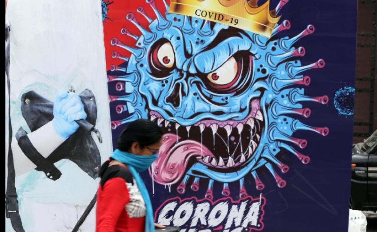 Una mujer pasa delante de un grafiti sobre el coronavirus Covid-19 pintado en una pared en Punjab (India).
