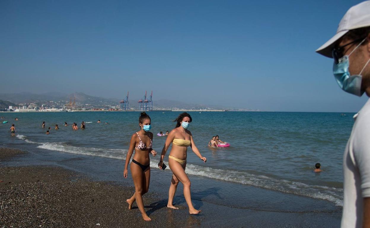 Unas chicas pasean por la playa de la Misericordia de Málaga con mascarilla