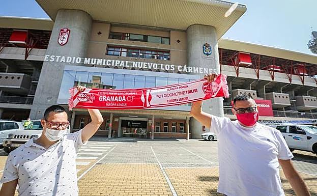 Dos aficionados del Granada sostienen una bufanda conmemorativa del partido en la puerta principal del estadio Nuevo Los Cármenes. 