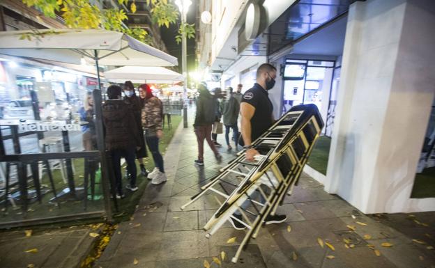 Un camarero recoge los taburetes de su establecimiento minutos antes de las 23.00 horas por el toque de queda. 