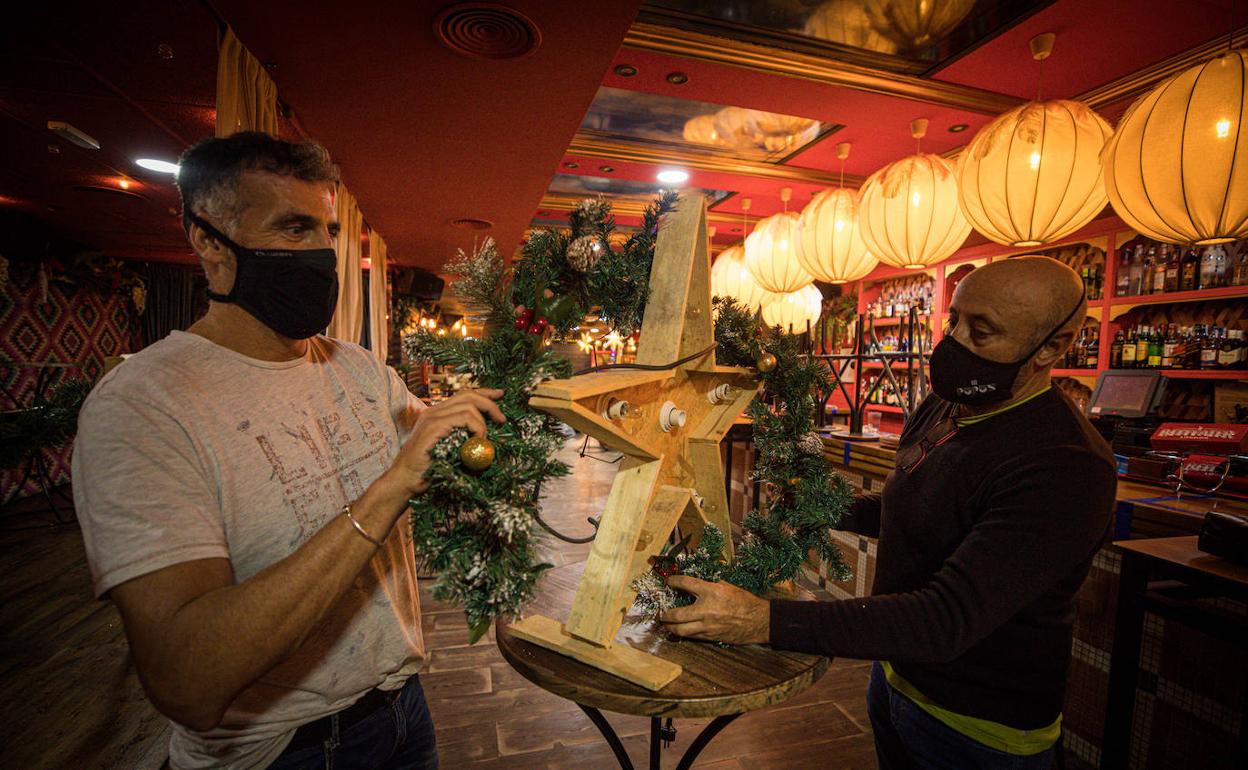 Dos trabajadores decoran el pub Ganivet, aún a la espera de saber si abrirá en Navidad.