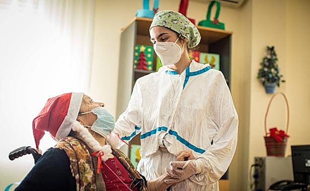 Una trabajadora, ataviada con el traje de protección, habla a una de las ancianas de Iznalloz. 