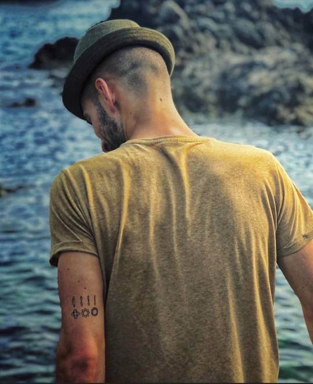Fernando, con un sombrero de espaldas y la teoría de cuerdas tatuada en su brazo izquierdo. 