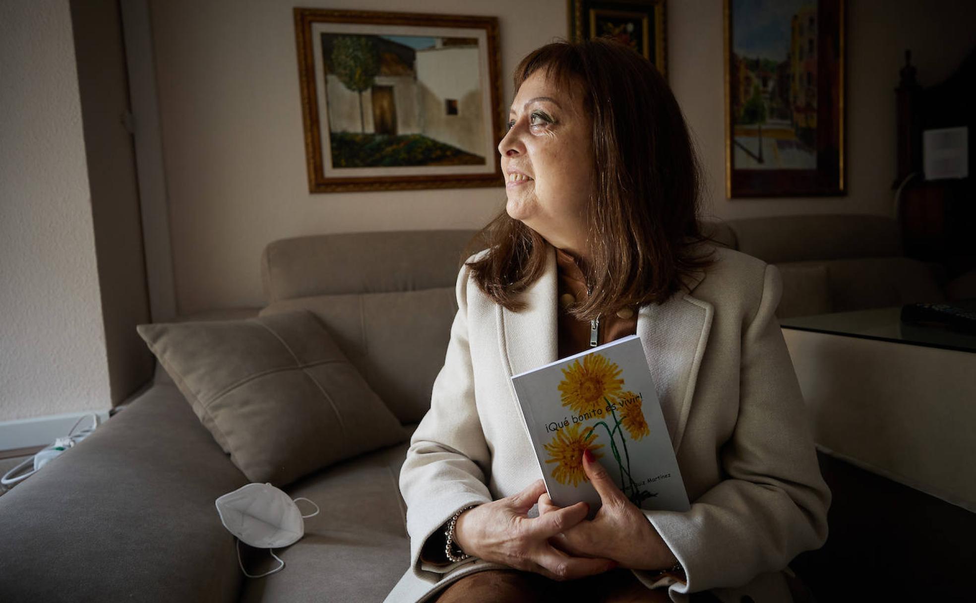 Mari Carmen Ruiz mira por la ventana de su casa, con su libro '¡Qué bonito es vivir!', entre las manos