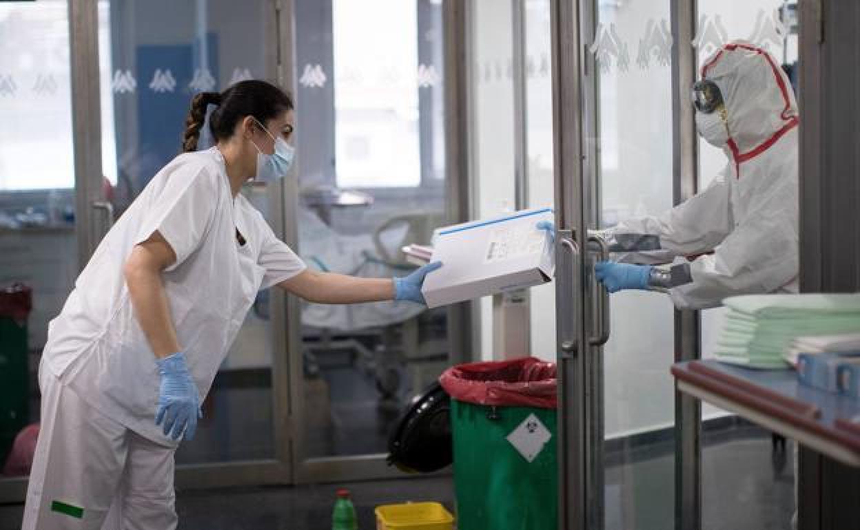 Una sanitaria entrega material a un compañero en la puerta de un box de la UCI de un hospital del SAS. 