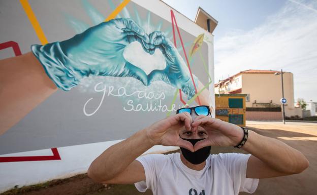El grafitero Badi Coloreando hace el gesto del corazón ante su mural en Cúllar Vega.