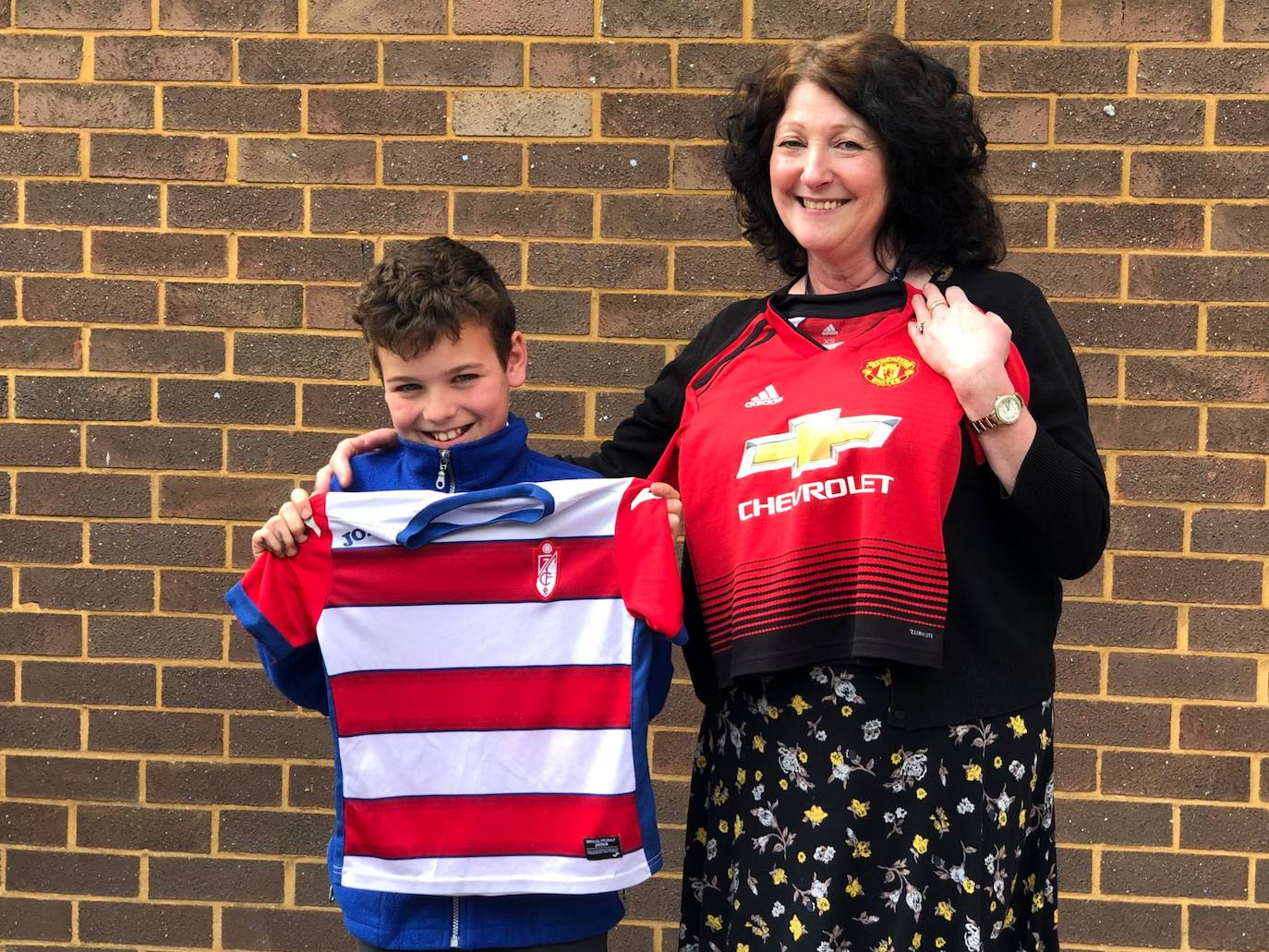 Ángel, hijo de Teresa, posa con su camiseta junto a una profesora del Manchester United en su colegio. 