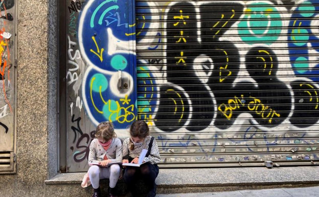 Dos niñas leen sendos libros sentadas en una calle del centro de Barcelona 