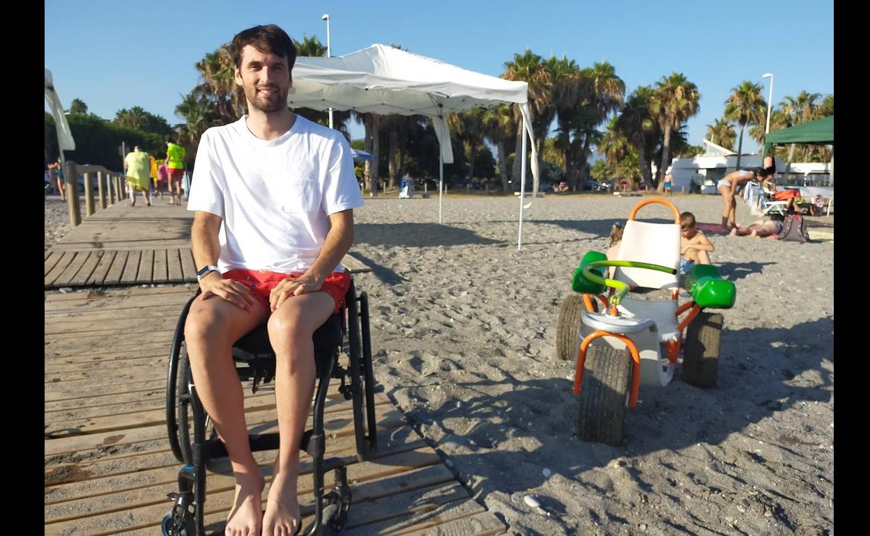 El joven motrileño, Daniel Rodríguez, posa en la pasarela de acceso a la playa junto a la silla anfibia. 