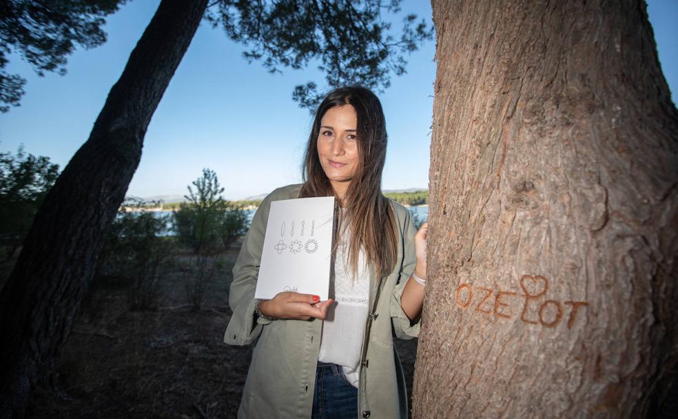 Patricia Valero muestra el libro que recopila toda la obra de su hermano Fernando, conocido como Ozelot, junto a un árbol que lleva marcado su nombre artístico en el Pantano de Cubillas. 