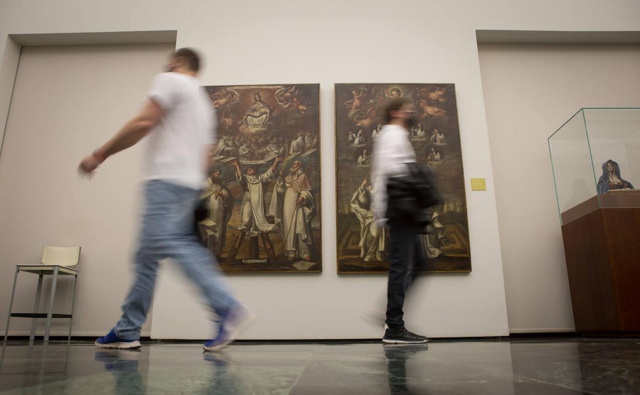Visitantes del Museo de Bellas Artes pasan por delante de dos de las obras que se exhiben con motivo de la exposición de José Risueño. 