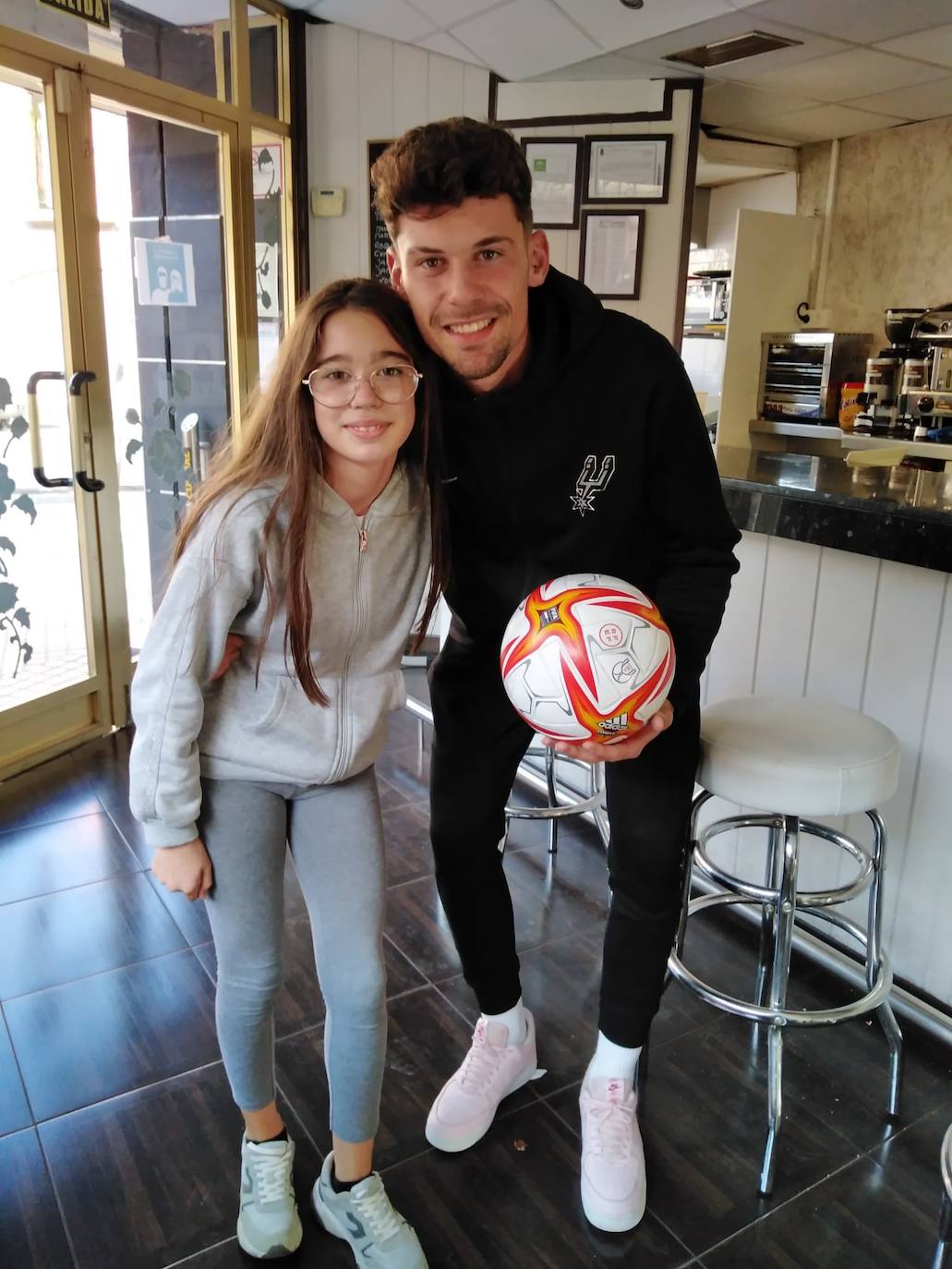 Adri Butzke posa ayer con el balón del partido por su 'hat-trick' junto a la hija de un cliente de la cafetería en la visita a sus padres. 