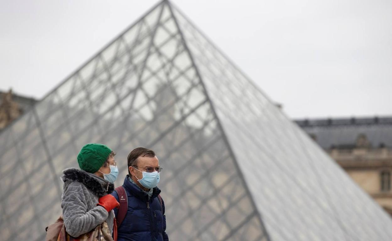 Dos turistas pasean con mascarilla ante el Museo del Louvre, en París.