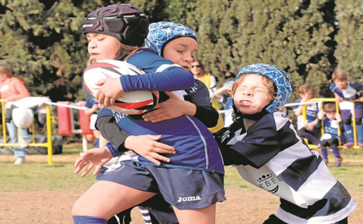 Dos jugadores de Rugby Málaga tratan de parar la carrera de un rival de Universidad.