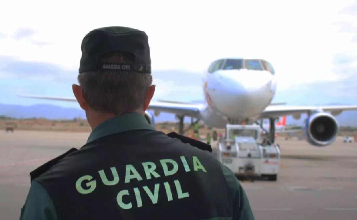 Un agente de la Guardia Civil, de espaldas, en la pista de un aeropuerto con un avión al fondo.