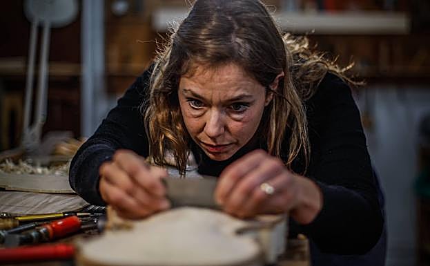 La luthier cepilla el cuerpo de un violín.