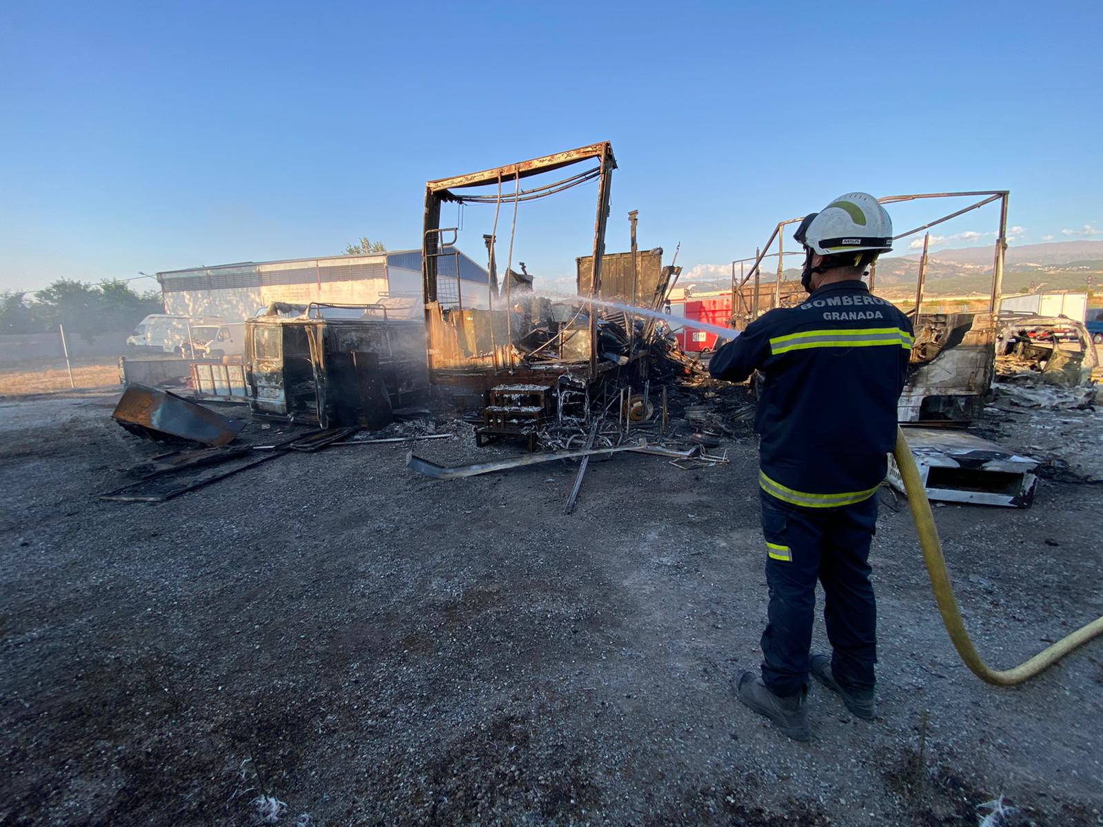 Un bombero lanza agua sobre los dos camiones y una de las furgonetas quemadas. 