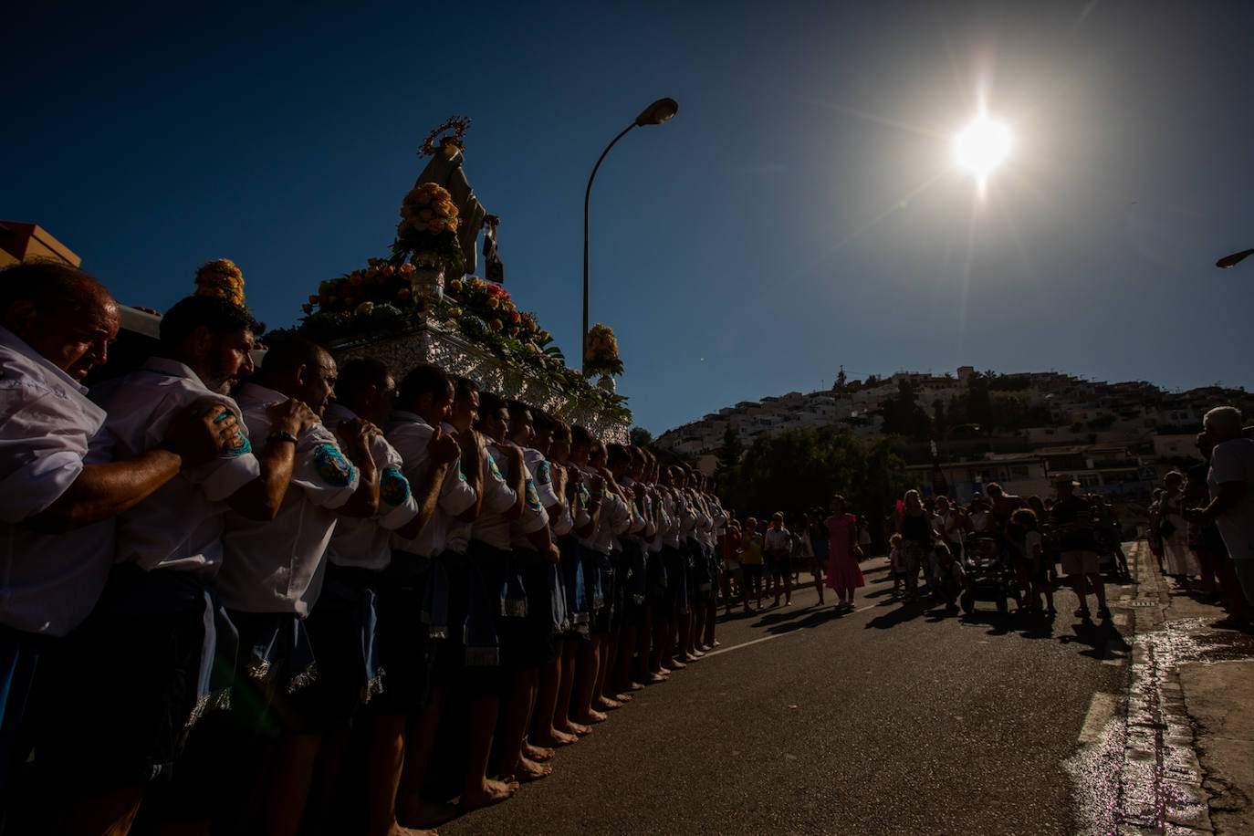 La Virgen del Carmen de Almuñéca, con el Barrio de Los Marinos al fondo, enfila la playa de San Cristóbal tras salir de la capilla.