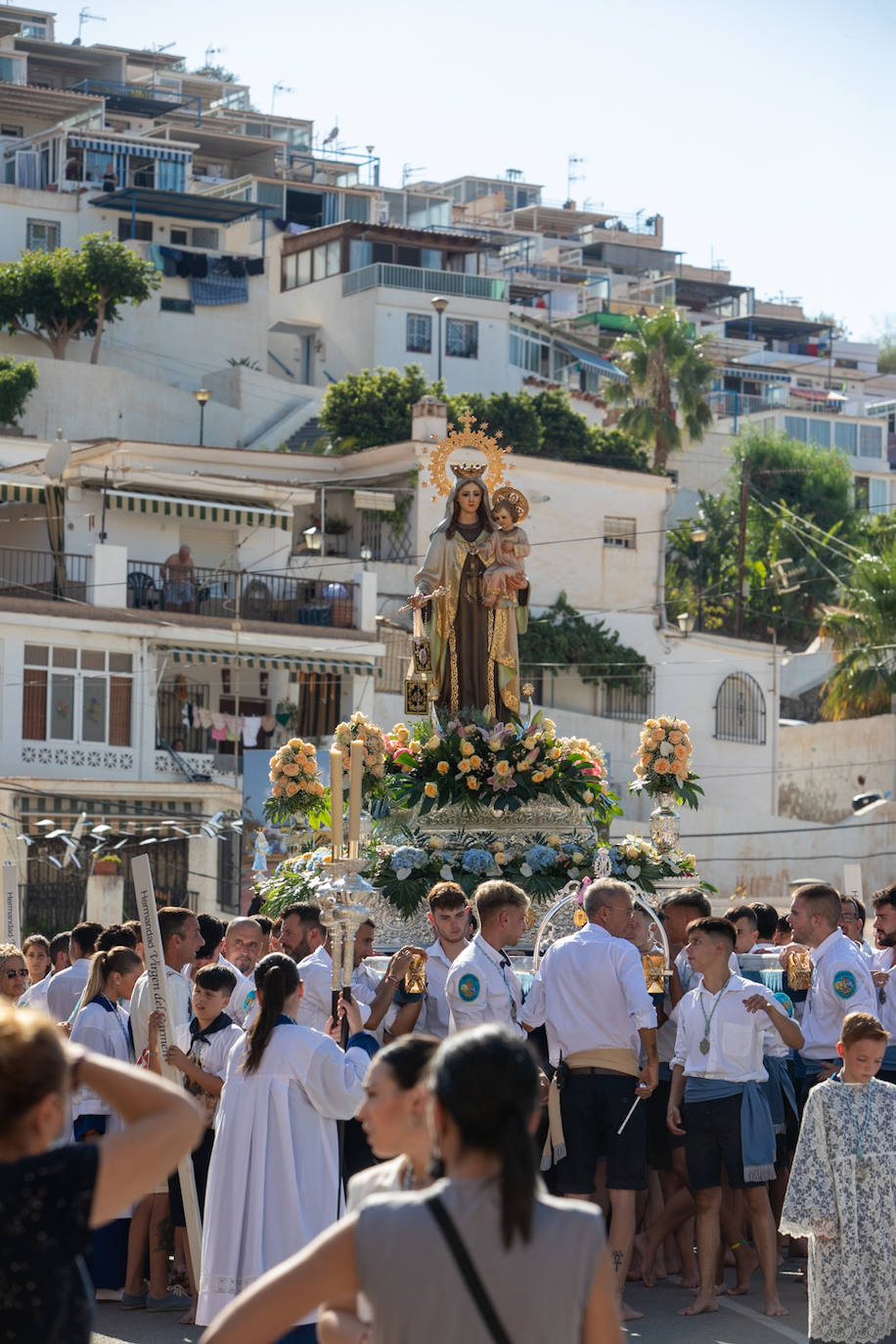 La Virgen del Carmen de Almuñéca, con el Barrio de Los Marinos al fondo, enfila la playa de San Cristóbal tras salir de la capilla.