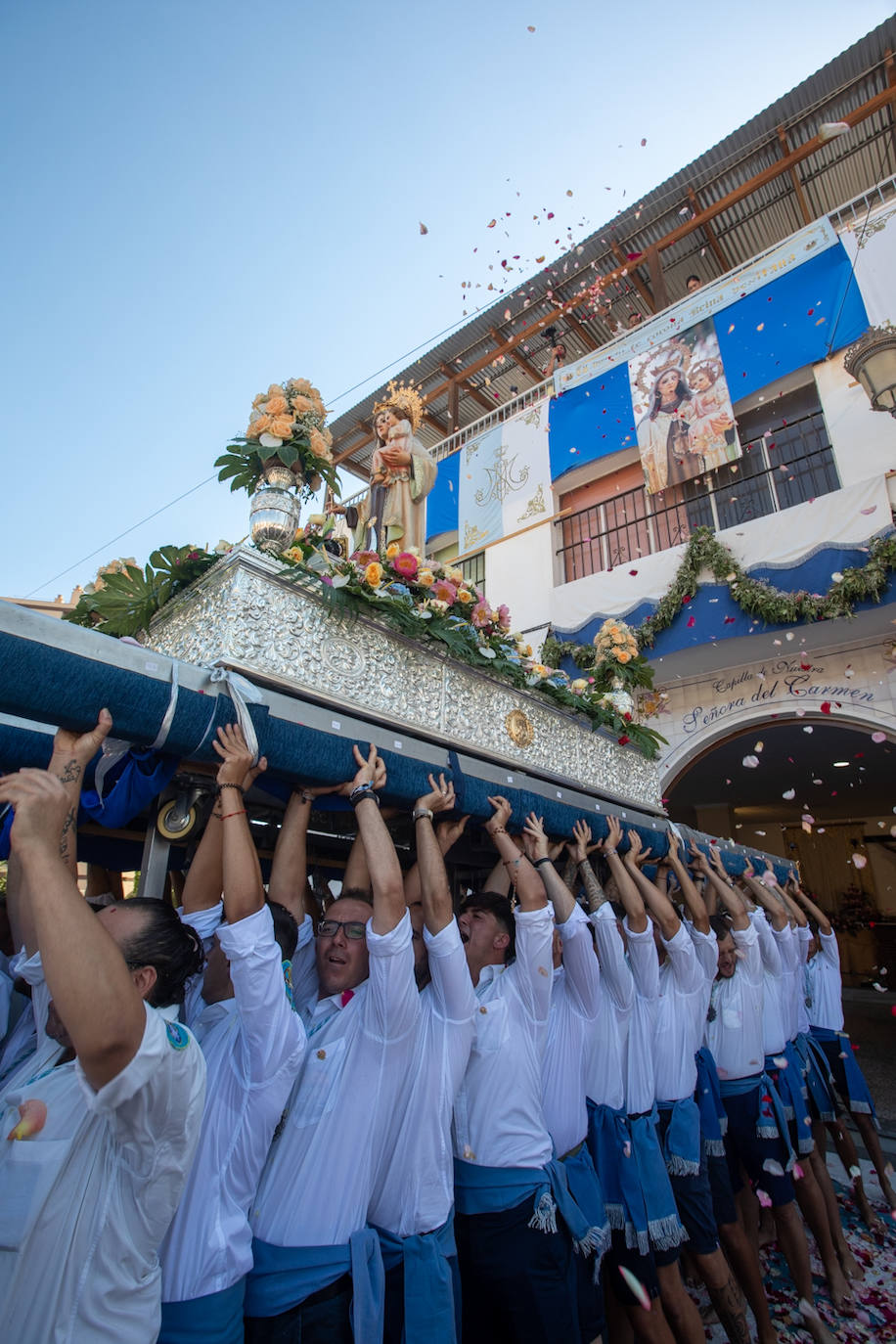 La Virgen del Carmen de Almuñéca, con el Barrio de Los Marinos al fondo, enfila la playa de San Cristóbal tras salir de la capilla.