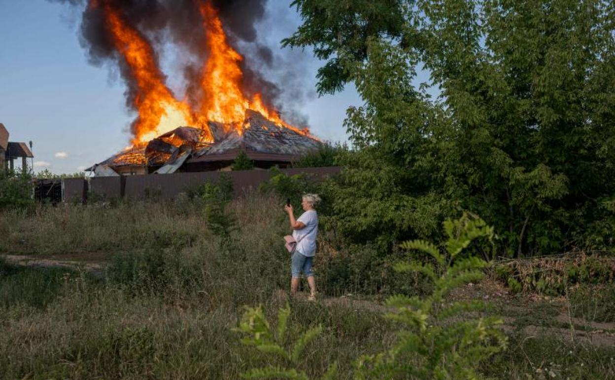 Una mujer hace una fotografía de una casa que arde tras un ataque. 