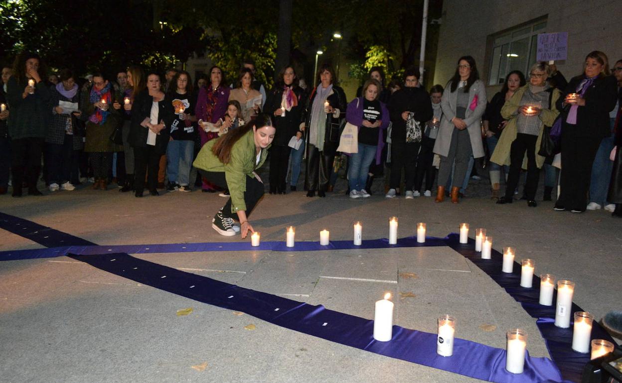 Una mujer deposita una vela sobre un lazo morado en recuerdo de las víctimas por violencia machista. 