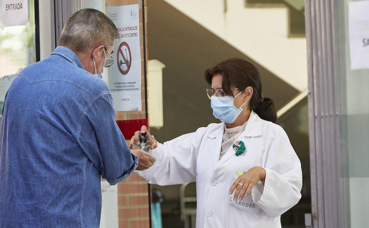 Una sanitaria dispensa gel hidroalcohólico a los pacientes que van a acceder al centro de salud. 