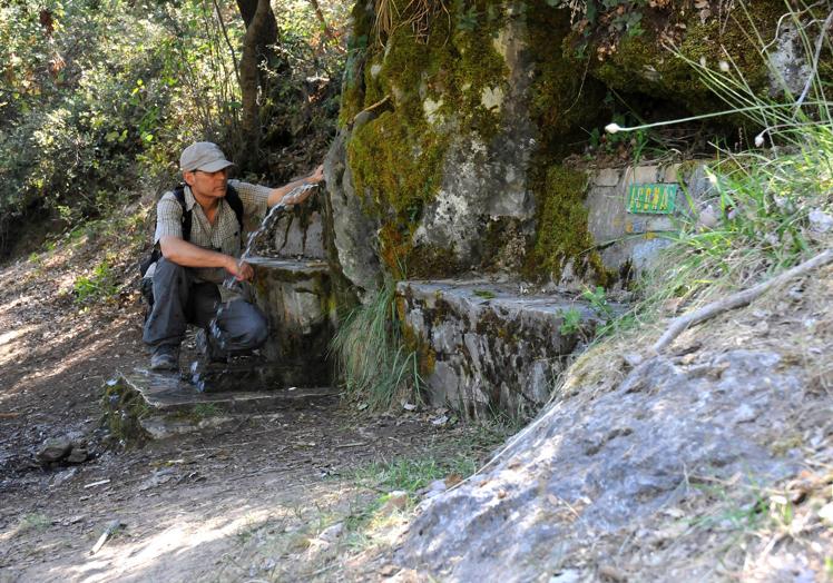 Un senderista bebe agua de la fuente de la Alfaguara.