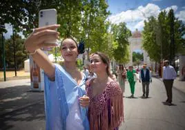 Dos jóvenes vestidas de flamenca se hacen una auto foto con la portada del ferial al fondo.