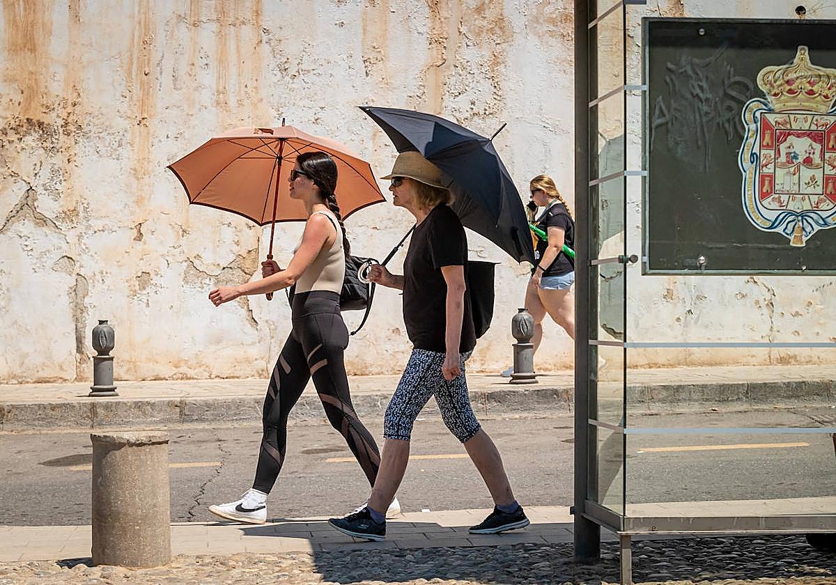 Dos personas pasean por la capital granadina usando parasoles durante un de las olas de calor de este mes de julio.
