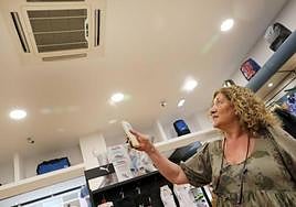 Una mujer regula la temperatura del aire acondicionado en un comercio.