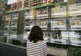 Una joven observa carteles de viviendas a la venta en un tablón.