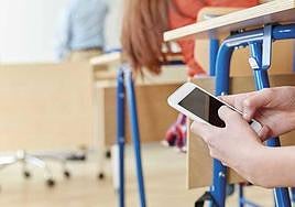 Un alumno manipula un terminal de telefonía móvil dentro del aula.