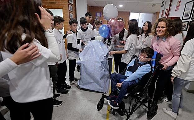 Imagen principal - Arriba, Martín delante de su regalo. Abajo, acarreando la silla y una alumna con el peluche mascota. 