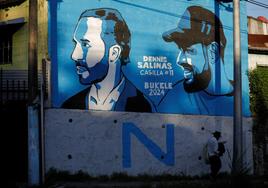 Un hombre camina junto a un mural que representa al presidente de El Salvador, Nayib Bukele.