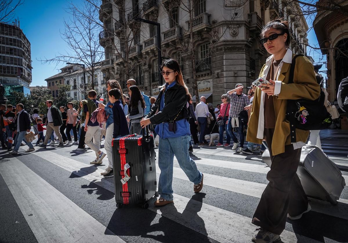 Turistas con sus maletas cruzan el paso de cebra de Gran Vía este sábado-