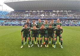 Formación inicial del Linares Deportivo en La Rosaleda, vistiendo de color olivo y AOVE, con aficionados de los dos equipos al fondo.