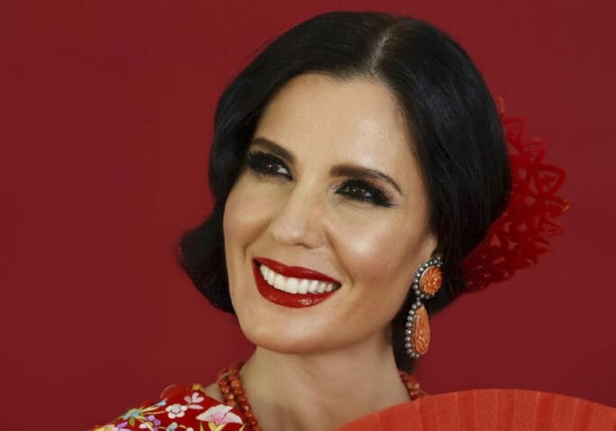 Diana Navarro, ataviada de un vestido rojo con flores y un abanico, se muestra sonriente.