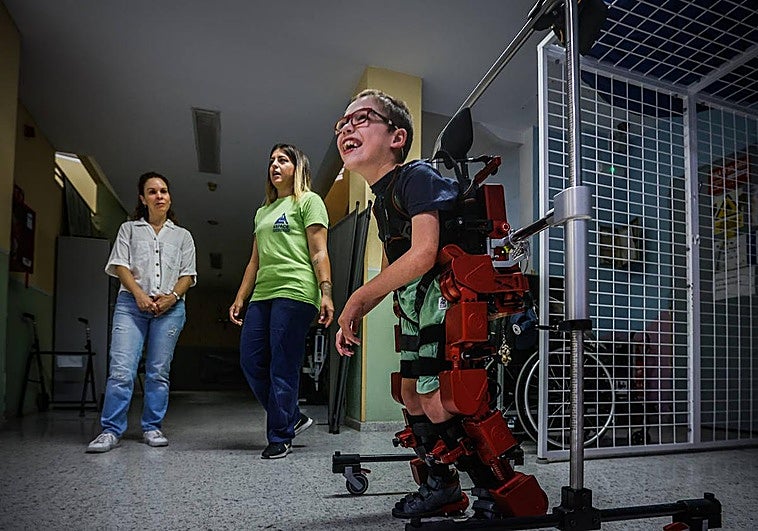 Mateo anda gracias al exoesqueleto en presencia de su madre y su fisio.