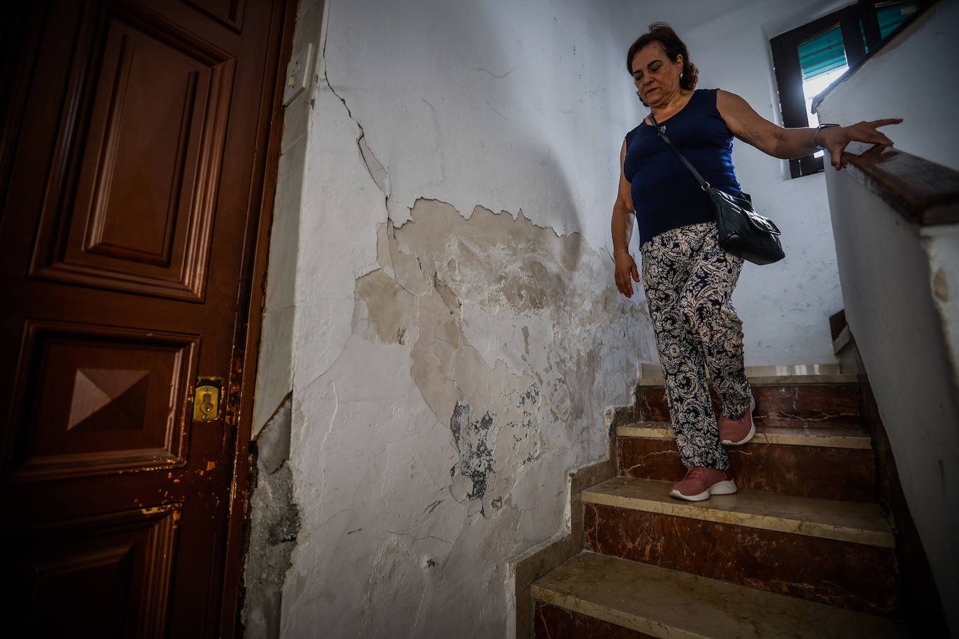 Una vecina baja las escaleras de un portal de calle Cataluña, con humedades y paredes agrietadas.
