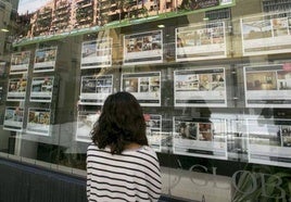 Una joven observa carteles en el escaparate de una inmobiliaria.