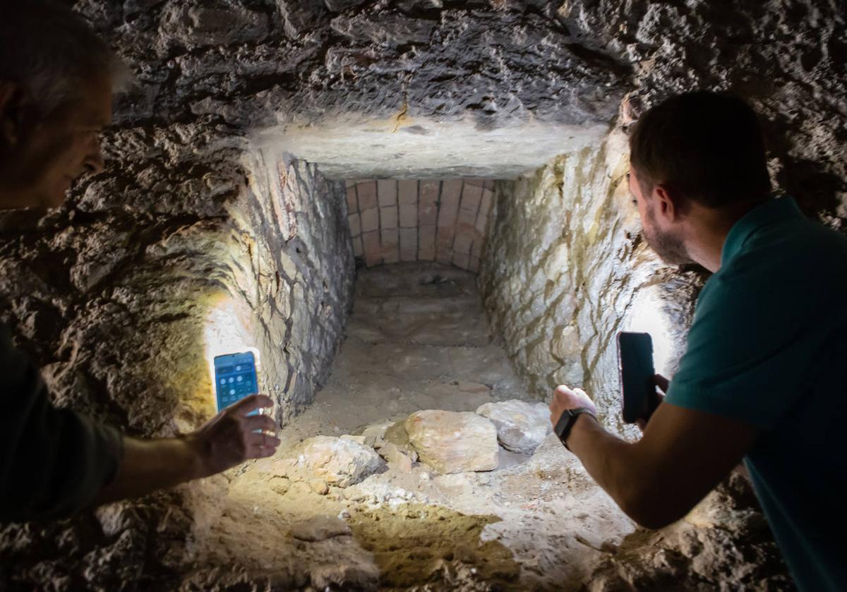 Manuel Moreno y Antonio Manuel Montufo iluminan con sus teléfonos móviles uno de los diez tragaluces que daban claridad al corredor y la sala cuadrada del criptopórtico de Las Gabias.