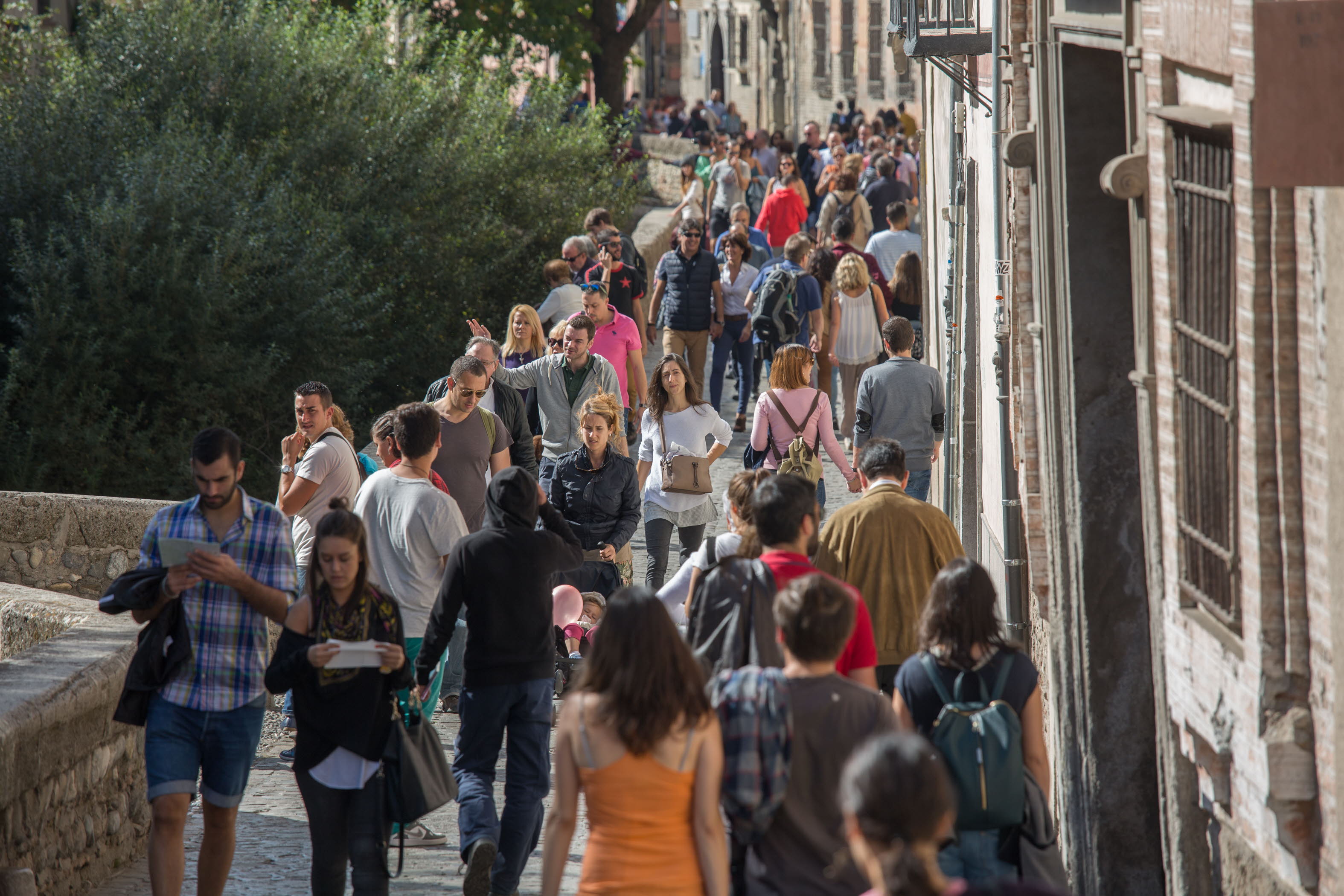 Decenas de turistas recorren el Paseo de los Tristes de Granada.