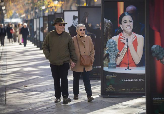 Una pareja camina por la Carrera de la Virgen, junto a las fotos de los Goya.