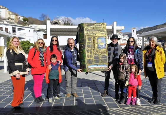 Varias personas mostrando el gigantesco libro cerrado en la plaza de Mecina Bombarón, que irá a FITUR