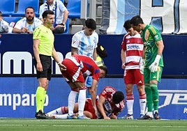 Los jugadores del Granada atienden a un dolorido Miguel Rubio en La Rosaleda.